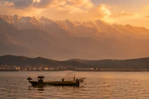 Erhai Lake at golden hour with the Cangshan mountain range in the background and a small fishing boat in the foreground