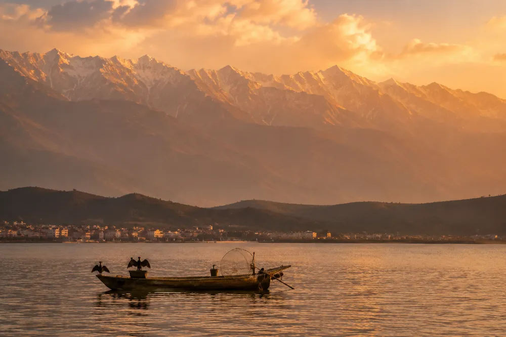 Erhai Lake at golden hour with the Cangshan mountain range in the background and a small fishing boat in the foreground