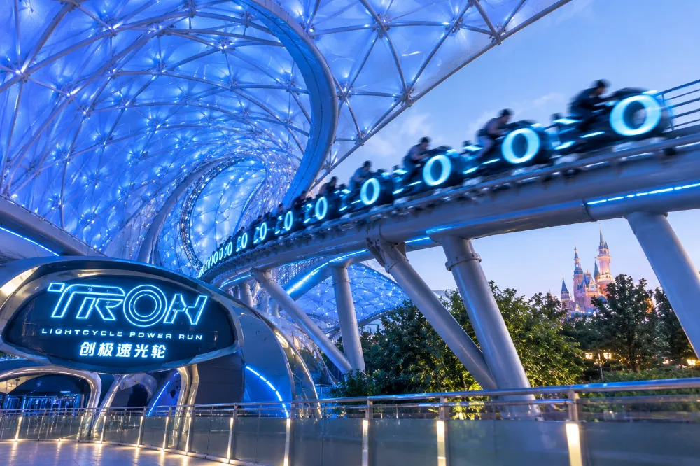 TRON Lightcycle Power Run coaster train mid-launch under its blue neon canopy at Shanghai Disneyland