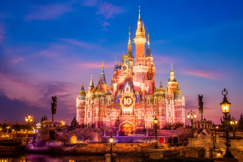 The Enchanted Storybook Castle at Shanghai Disneyland lit up with 10th anniversary projection mapping in golden and rose colors