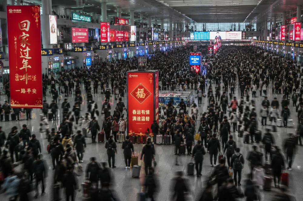 A packed Chinese train station concourse during the Spring Festival 2027 travel rush with travelers carrying luggage